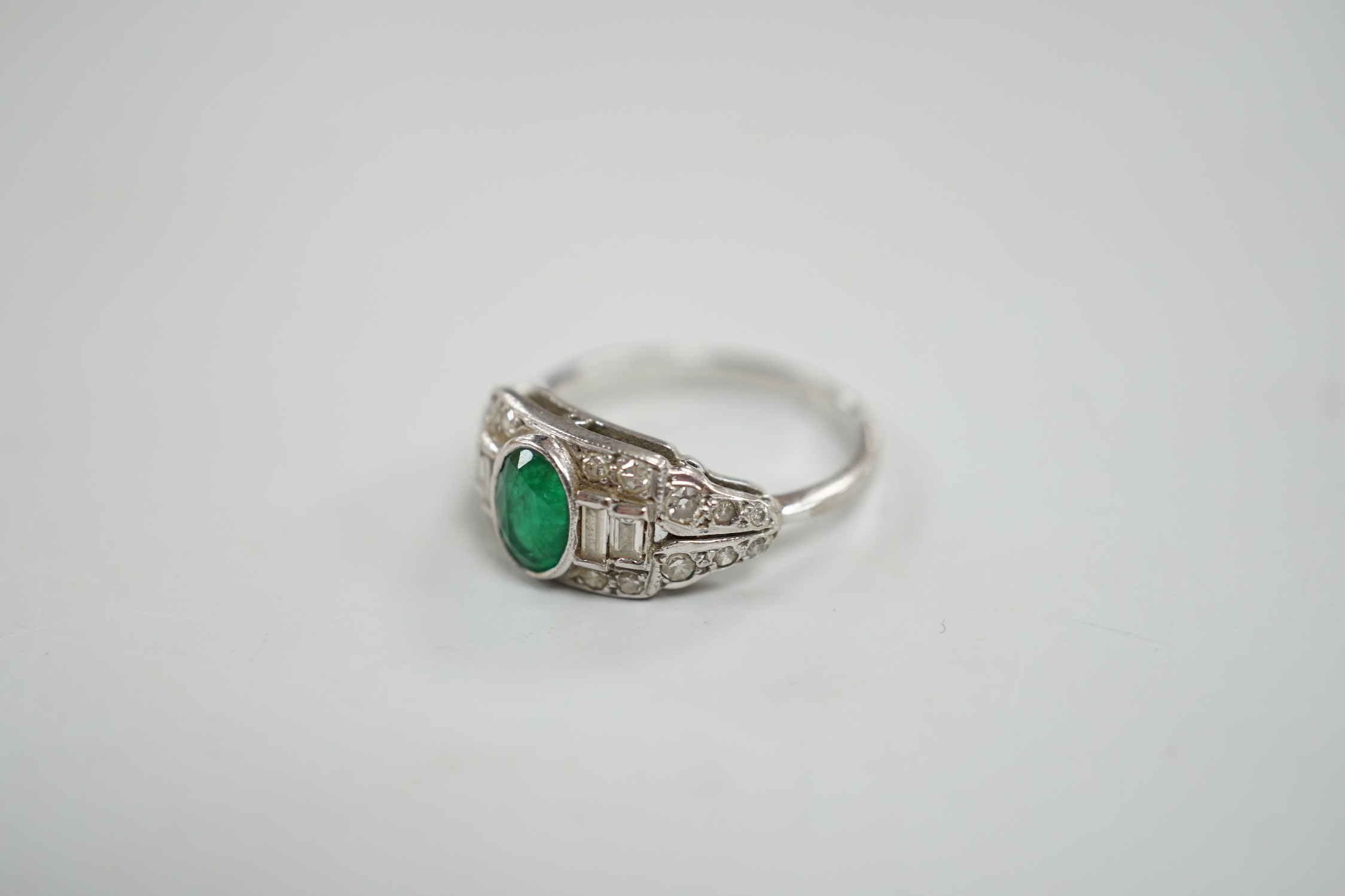 An Art Deco white metal, singe stone oval cut emerald and round and baguette cut diamond cluster set ring, size O/P, gross weight 4.2 grams.